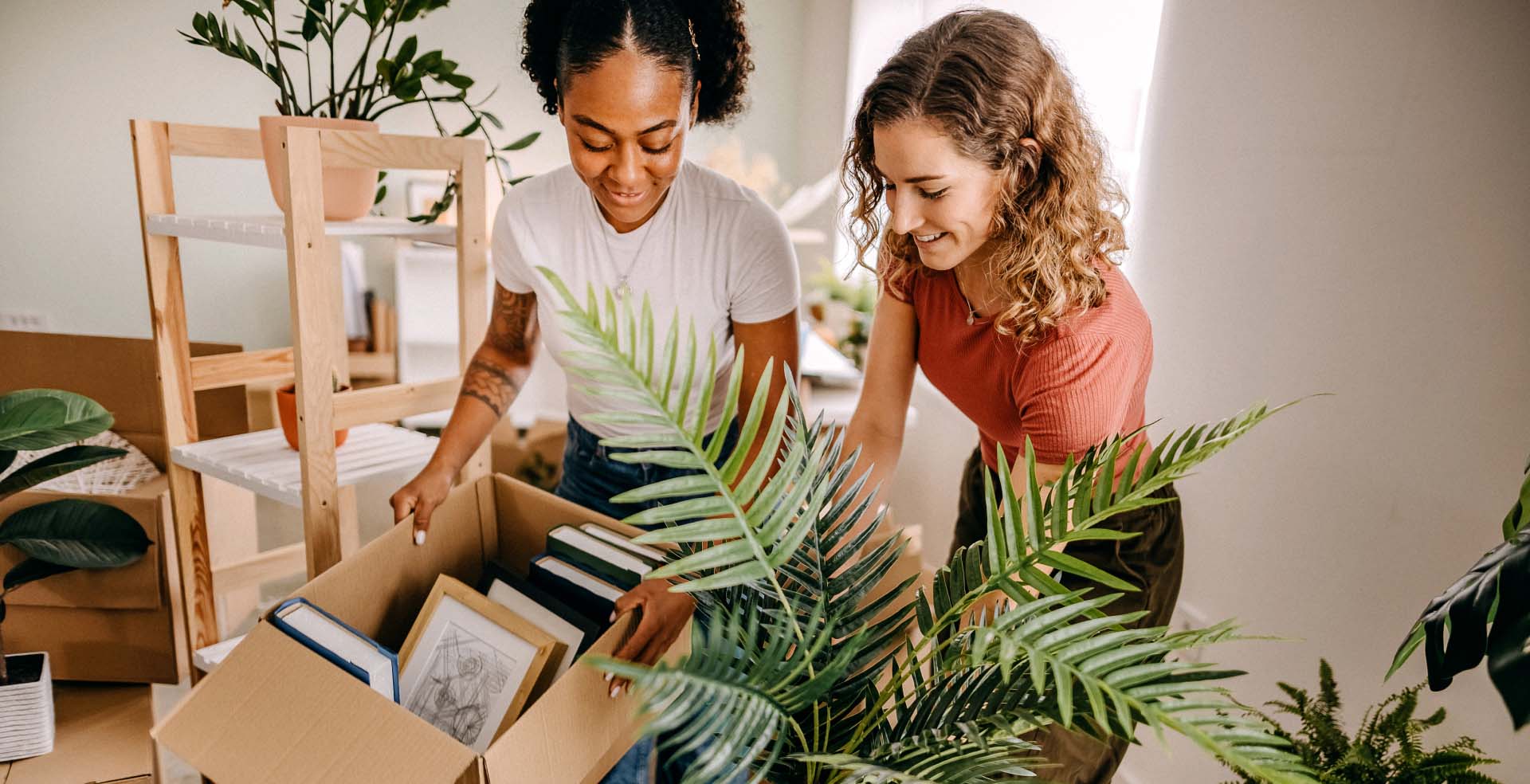 Two women unpacking moving boxes in a bright apartment.