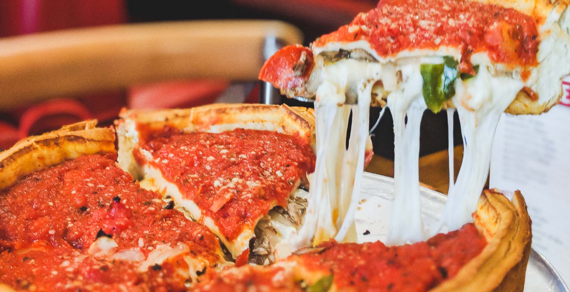 A slice of deep-dish pizza being pulled from a large pizza.