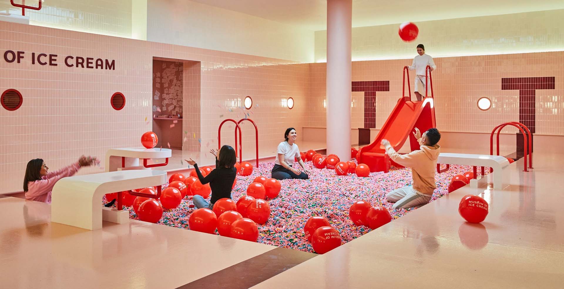 People playing in a shallow pool filled with sprinkles and red beach balls at Chicago's Museum of Ice Cream.