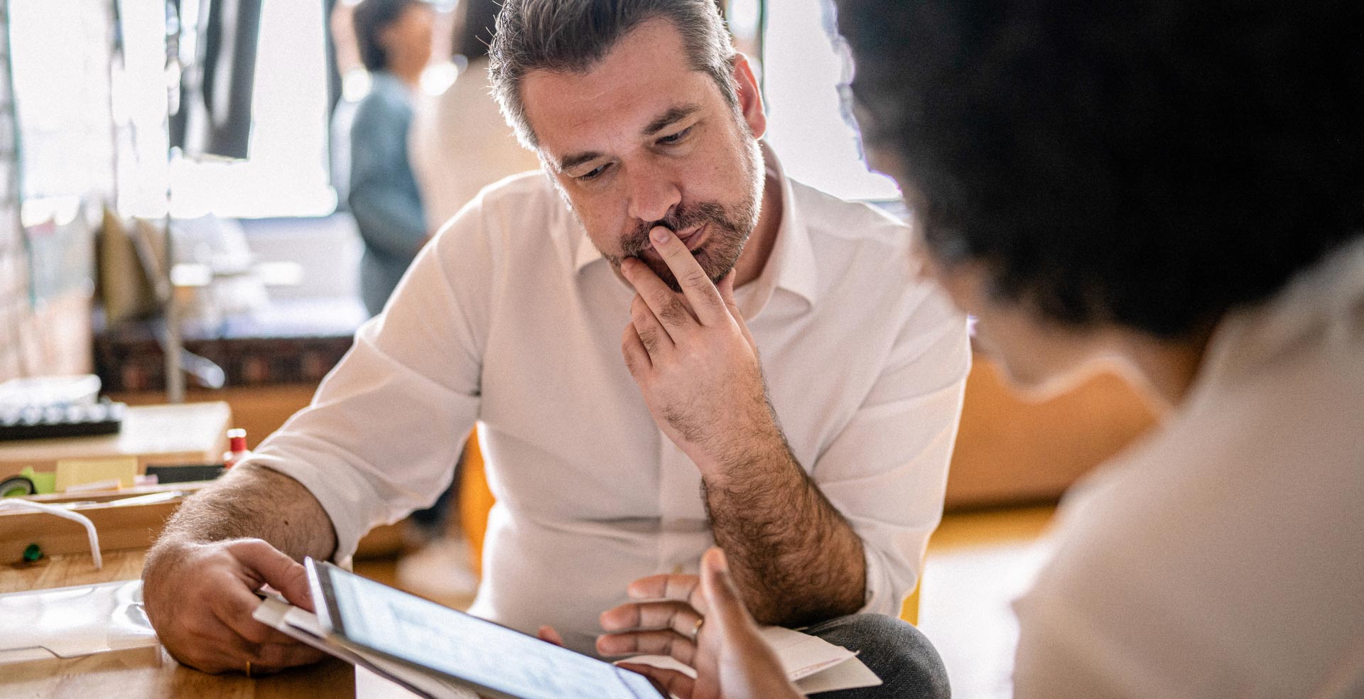 A man and a woman studying a computer tablet the man is holding.