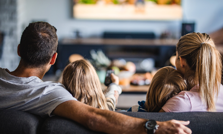 A man, woman, and two children watching T.V from their couch.