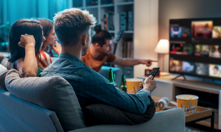 Two men and two women sitting on a couch choosing a movie from a streaming service.