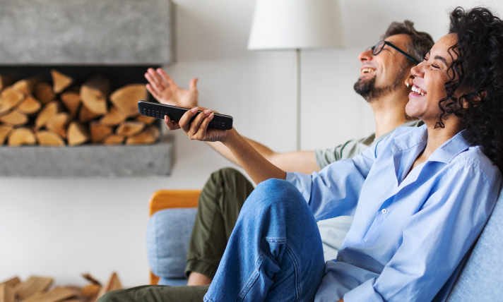 A man and a woman, who is holding a T.V remote control, laughing at what they are watching on T.V.