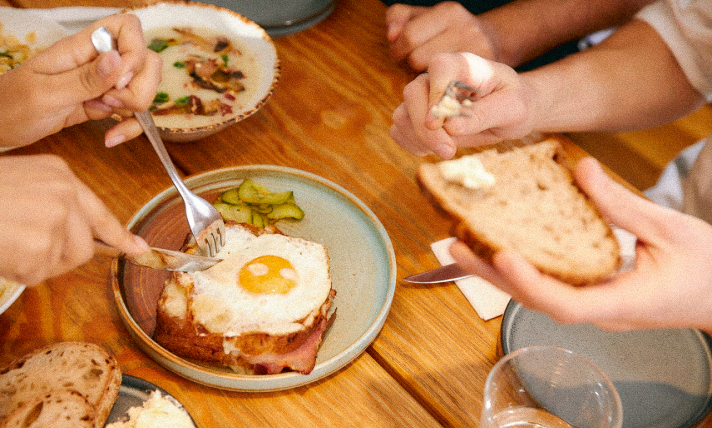 Three people sharing plates of breakfast food at a restaurant.