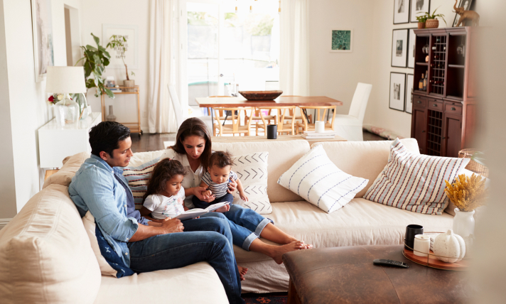 A man, a woman, a little girl, and a baby reading a book while sitting on a couch.