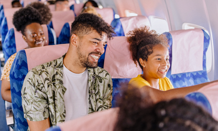 A man and a little girl sitting in an airplane and smiling.