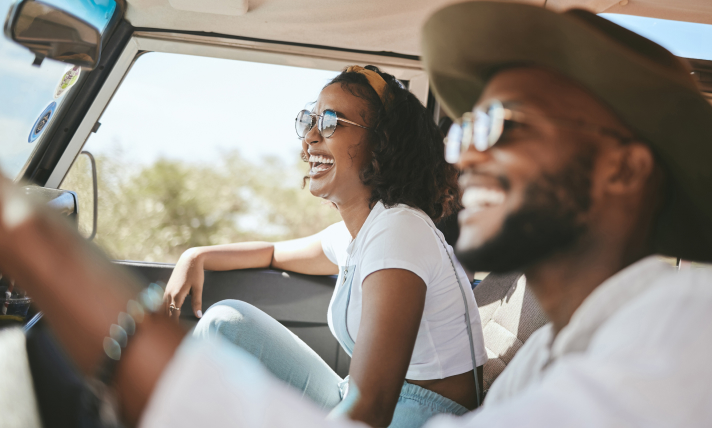 A man and a woman in a car smiling as the man drives the car.