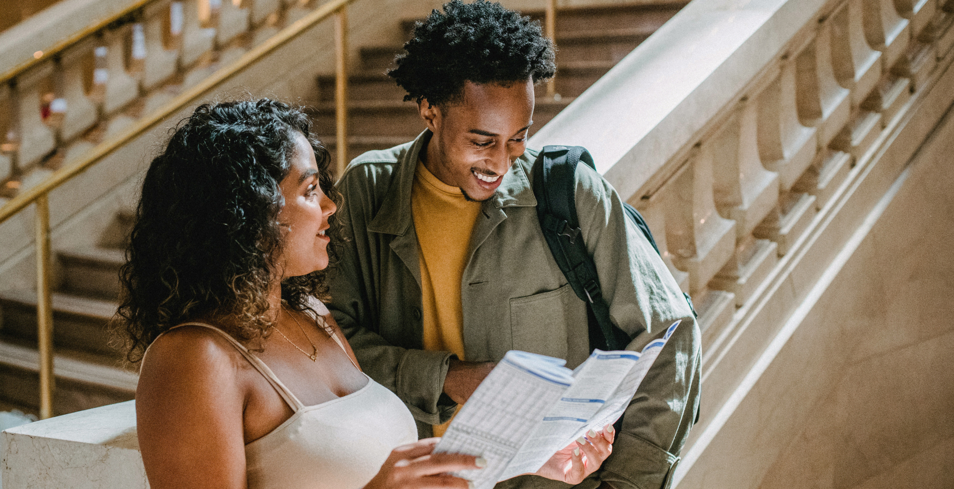 A man and a woman standing at the bottom of an ornate stone staircase studying a map and smiling.