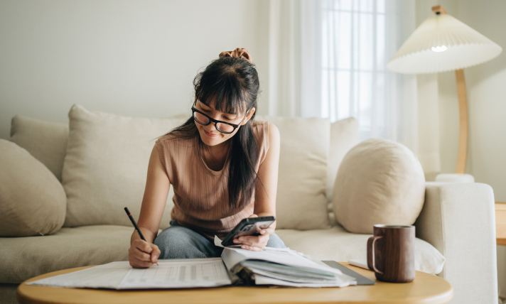 A woman sitting on her couch and writing in a notebook.