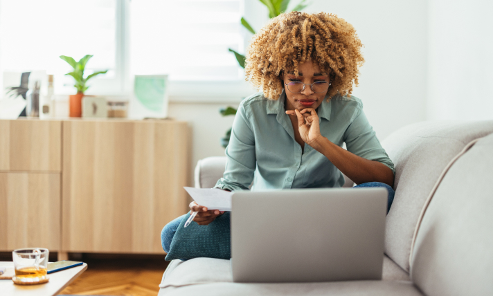 A woman sitting on a couch and reading from a laptop.