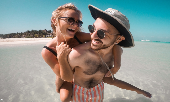 A woman being carried on a man's shoulders at a sunny beach.