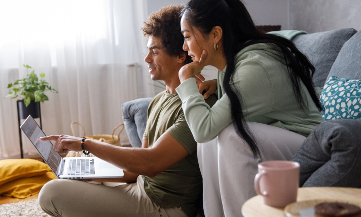 A man and a woman discussing what the man is pointing at on a laptop screen in front of them.