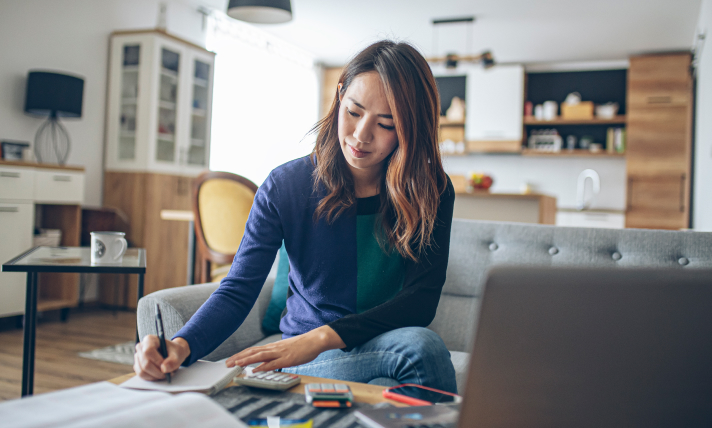 A woman sitting on a couch writing in a notepad.