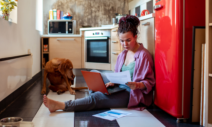 A woman sitting on her kitchen floor reading a piece of paper.