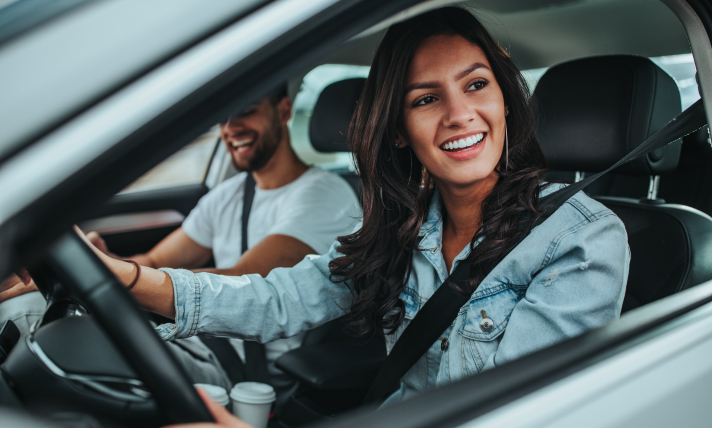 A man and a woman smiling as they drive in a car.