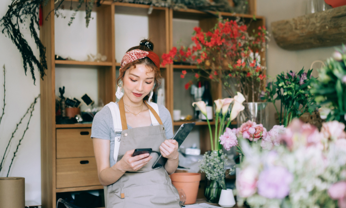 A woman standing behind the corner of her shop reading from her smartphone.