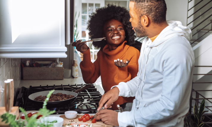 A man and a woman smiling while cooking a meal together.