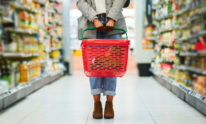 Close-up of a woman holding a red shopping basket in a grocery store aisle.