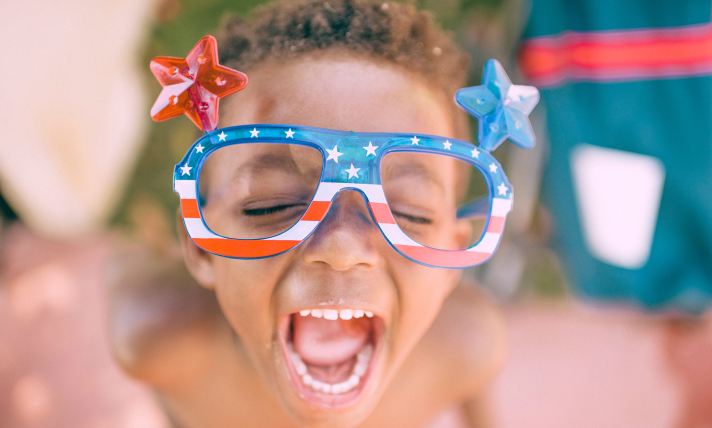 Close-up of a little boy wearing Fourth of July sunglasses and laughing.