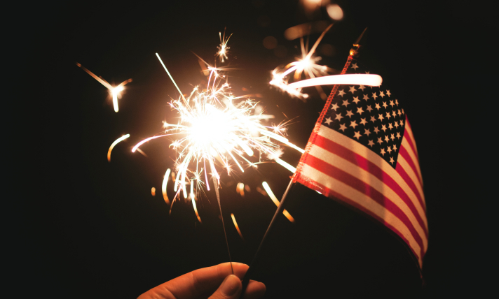 Close up of a sparkler and an American flag.