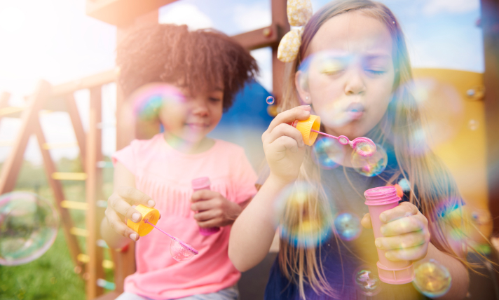 Two girls blowing bubbles outside.