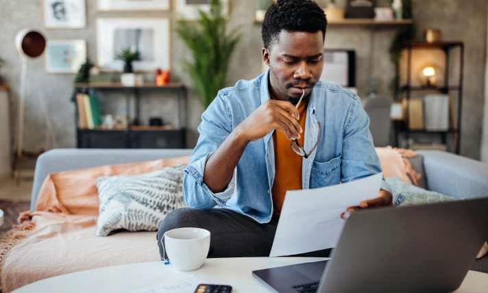 A man sitting on a couch reading a piece of paper.