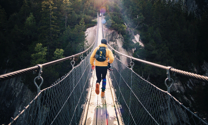 A man running across a suspension bridge in the forest.