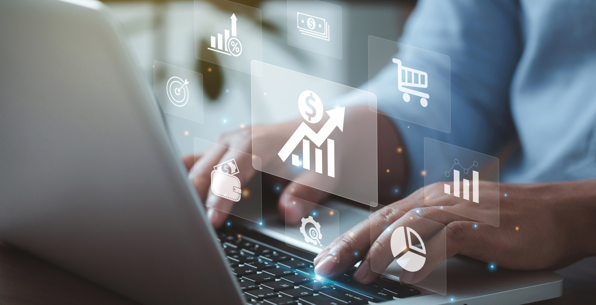 A man typing on a laptop keyboard with various silver financial icons superimposed in front of his screen.