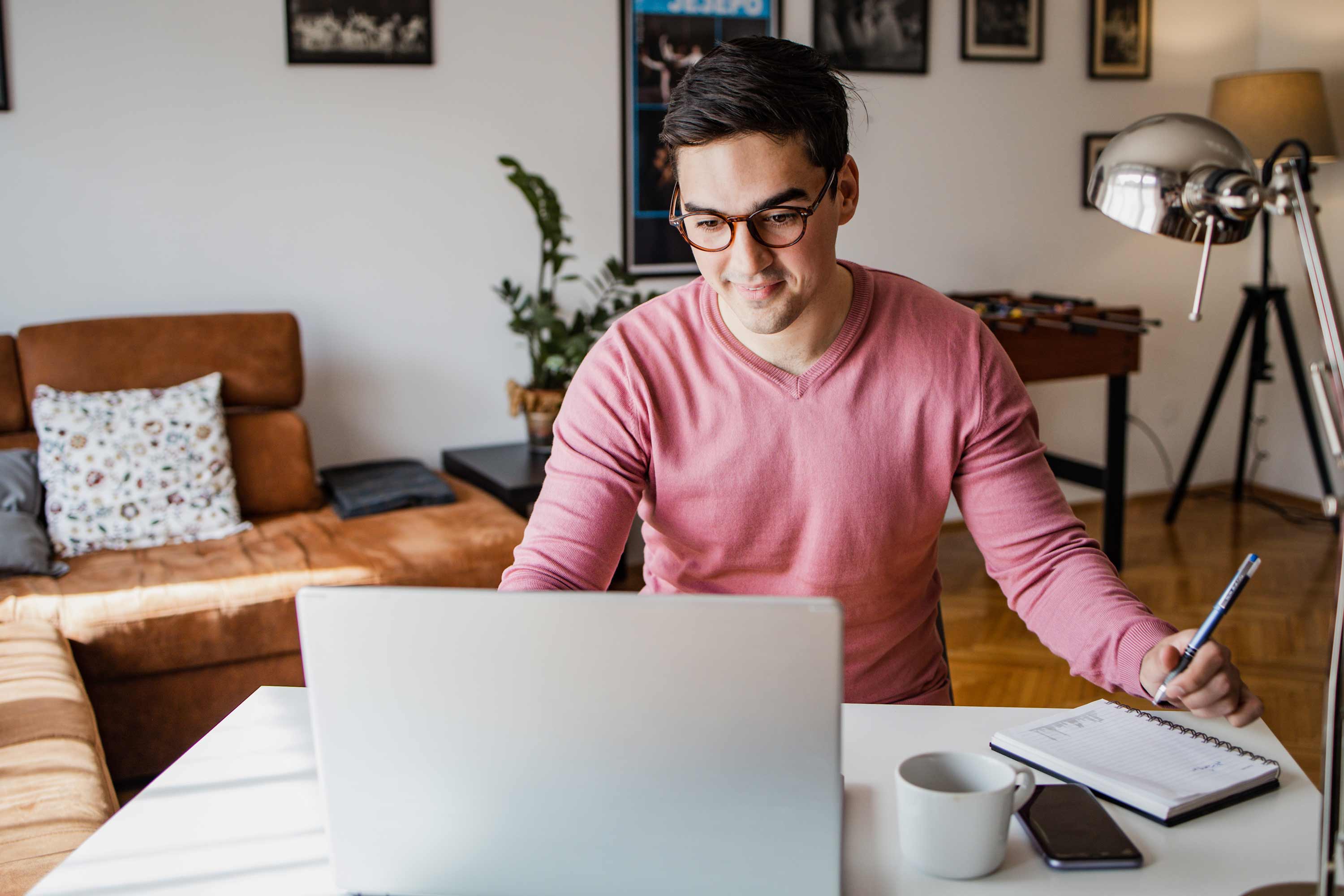 A man at a desk looking at his laptop and smiling.