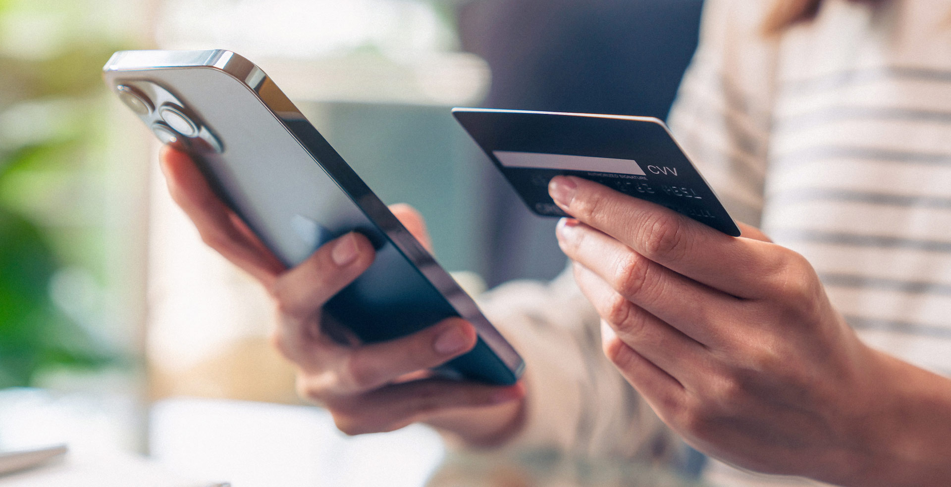 Close-up of a woman holding her phone in one hand and a credit card in her other hand.