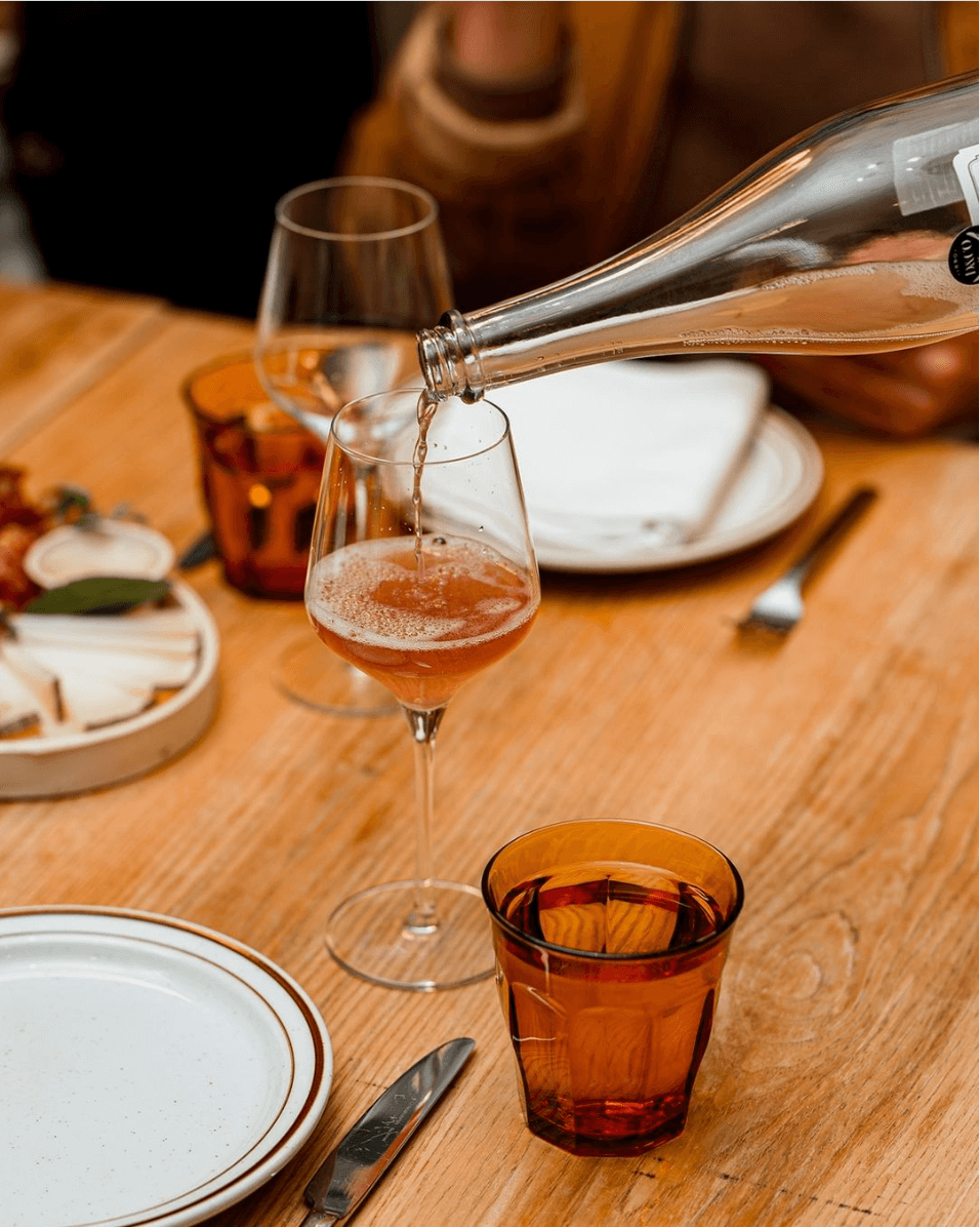 Rose wine being poured from a bottle into a glass on a table laid with plate and cutlery.