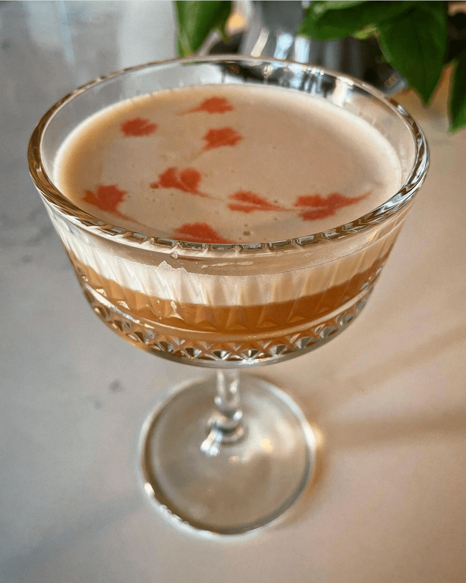 A cocktail with foam top and red heart pattern on the foam in a tall stemmed cocktail glass.